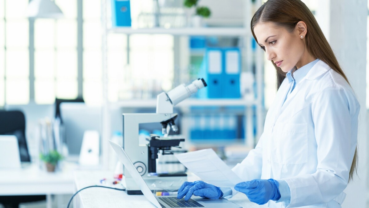 Young female scientist using laptop and microscope in laboratory.
