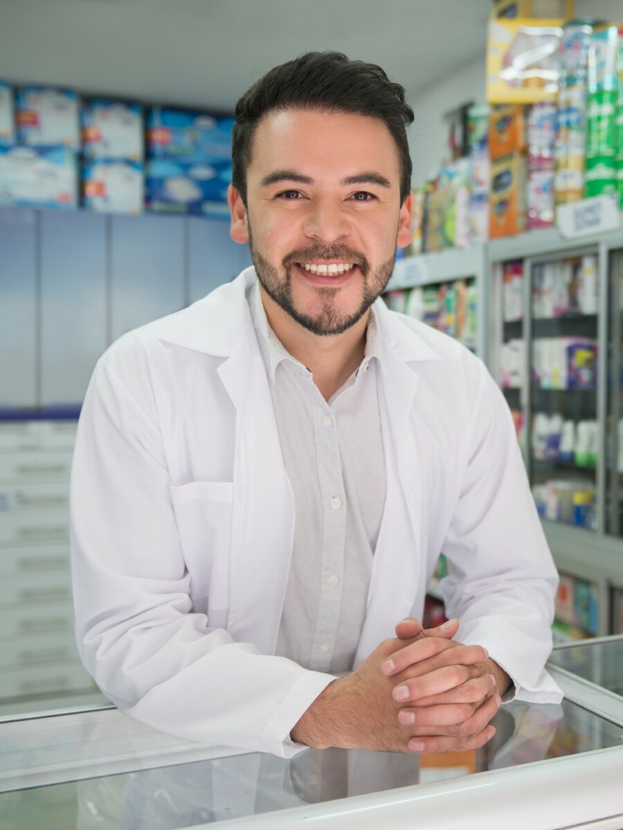 Portrait of handsome male pharmacist leaning elbows on counter while smiling at camera very cheerfully - Healthcare concepts